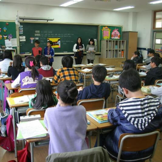 School kids in classroom at school watching four students give a presentation at the front of the class.